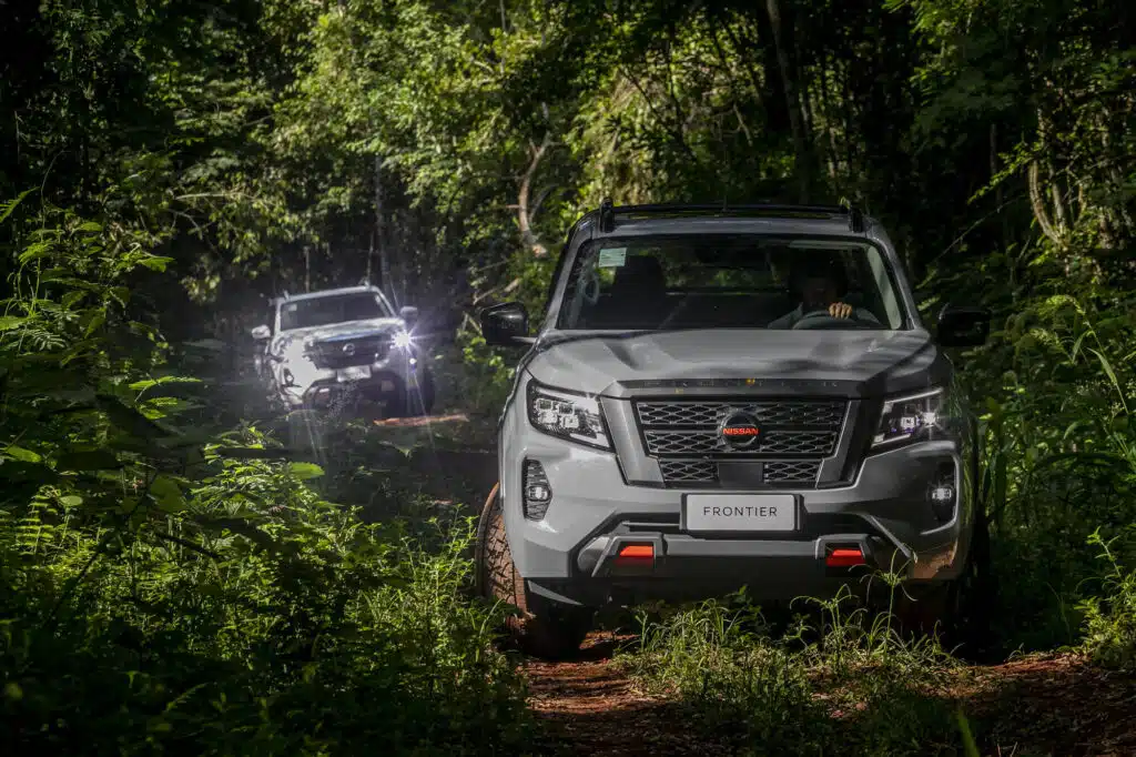 Duas picapes Nissan Frontier percorrem trilha em área de mata