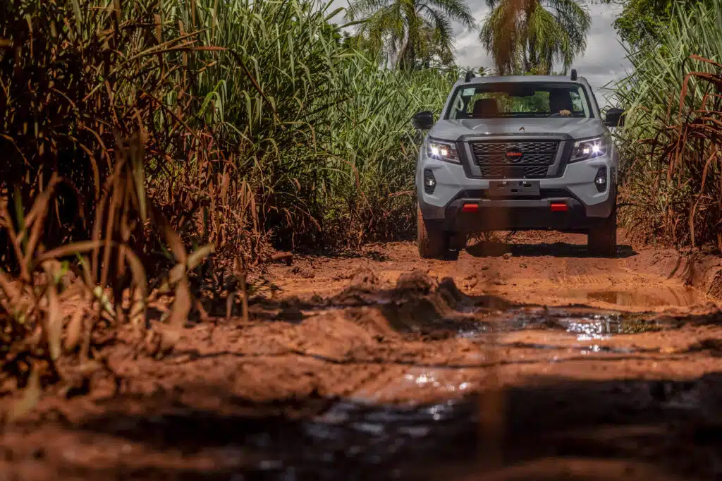 Nissan Frontier circula por estrada de terra cercada por vegetação